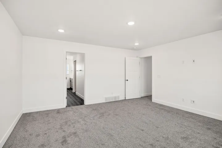 Spacious bedroom featuring neutral white walls, recessed ceiling lighting, and plush carpeting throughout