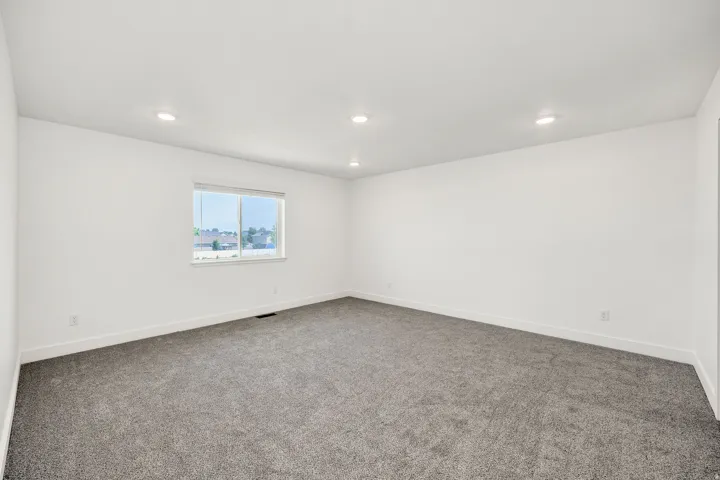 Spacious room featuring neutral white walls, recessed ceiling lighting, and soft gray carpet flooring