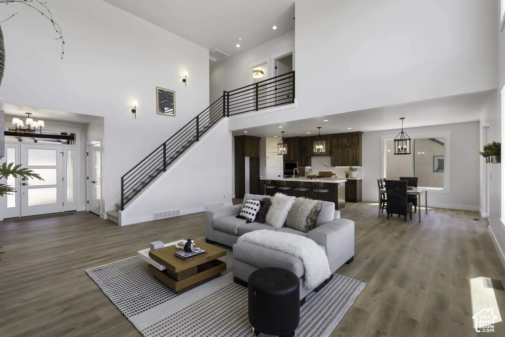 Two-story living area with high ceilings, wood-finish flooring, and a modern staircase with black metal railings