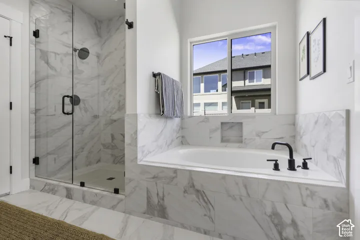 Spacious bathroom featuring a glass-enclosed shower, a built-in soaking tub with a matte black faucet, and extensive marble-look tile
