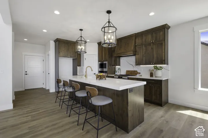 Gourmet kitchen with wood-finish flooring, a large center island, dark wood cabinetry, a built-in range hood, and pendant lighting