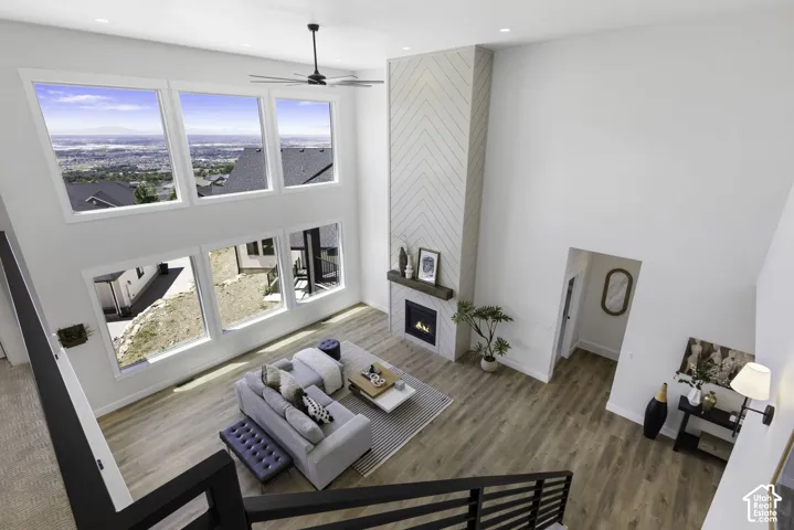 Soaring two-story living space with expansive multi-pane windows showcasing expansive landscape vistas, warm wood-finish flooring throughout, and a gas fireplace with stone surround