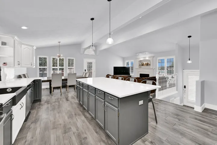 Spacious kitchen featuring an extended island with white countertop, wood-finish flooring, two-tone cabinetry, stainless steel appliances, and integrated dining area