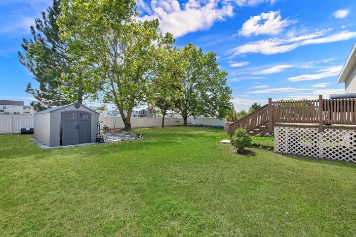 Expansive backyard featuring a wood deck with lattice skirting, a storage shed on a concrete pad, mature trees, and a privacy fence