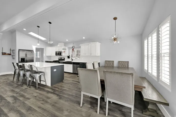 Spacious kitchen and dining area featuring wood-finish flooring, white cabinetry, a large kitchen island with counter seating, and plantation shutters