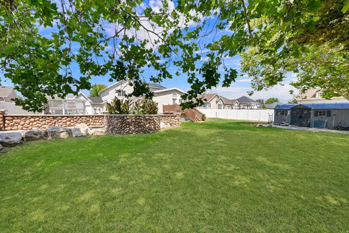 Expansive grassy yard with a stone retaining wall and a separate storage structure