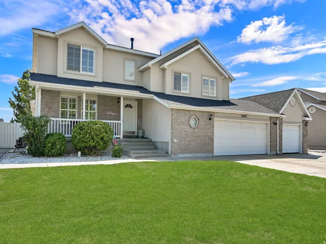 Stucco and brick exterior with a covered front porch, white railings, and a two-car garage
