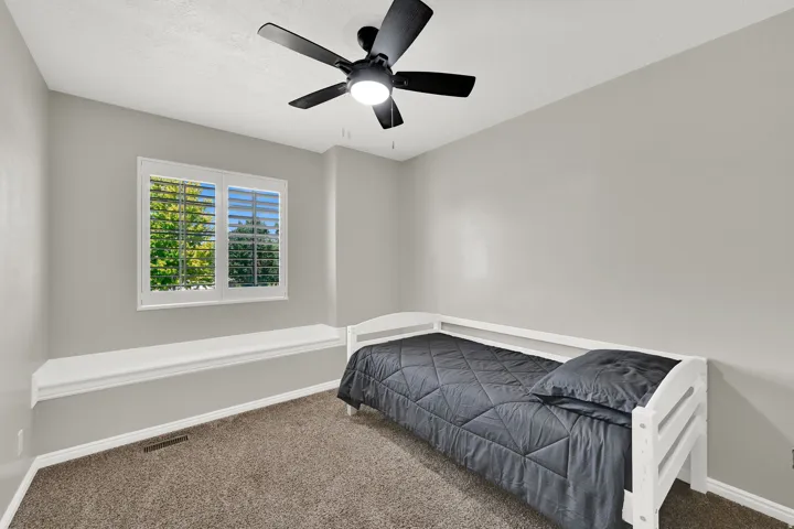Window with plantation shutters, integrated window bench, ceiling fan with light fixture, and carpet flooring
