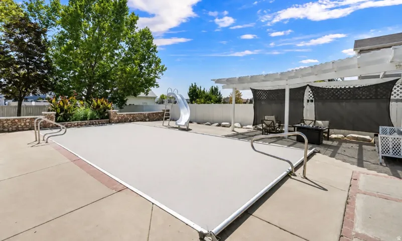 Outdoor pool area with a covered pool, concrete patio, a pergola with lattice panels, and a stone-clad planter
