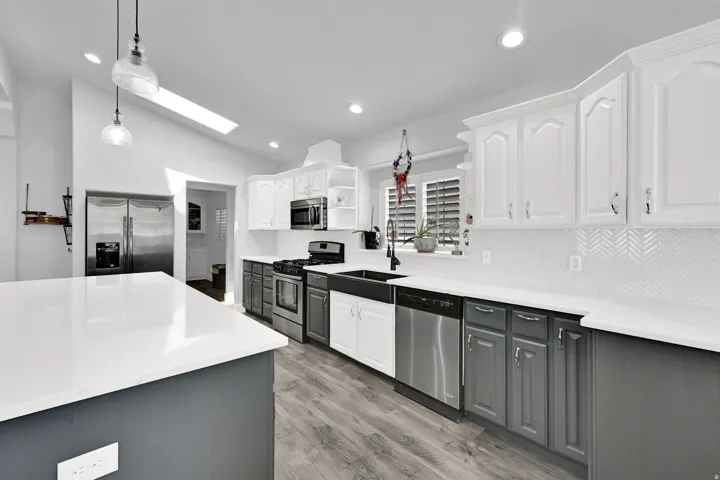 Kitchen featuring a skylight, recessed lighting, wood-finish flooring, two-tone cabinetry, and stainless steel appliances