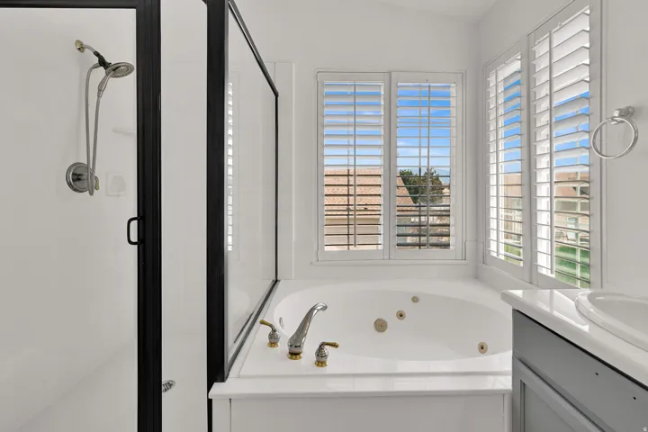Shower enclosure with black framing, jetted soaking tub, plantation shutters, and a vanity with an integrated sink