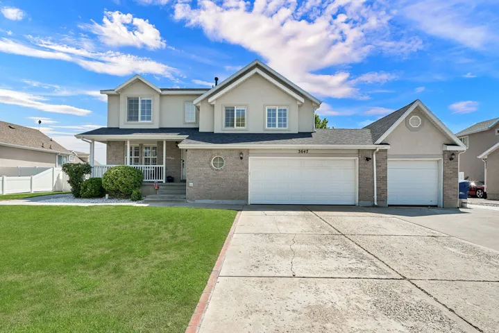 Two-story residence featuring a covered front porch, brick and stucco exterior, multiple front-facing windows, an attached two-car garage, and an additional attached single-car garage