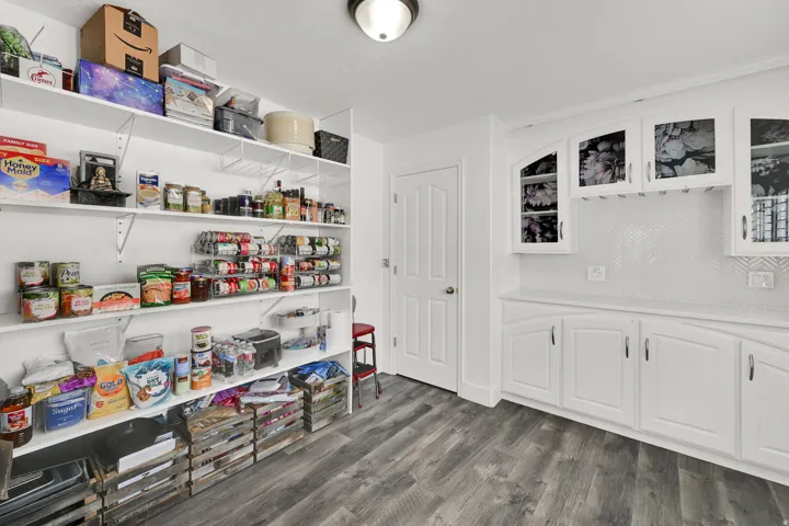 Extensive open shelving, white cabinetry with integrated glass-front display, white herringbone tile backsplash, and wood-finish flooring