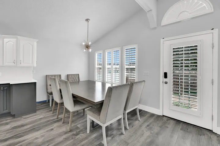 Vaulted ceiling with decorative beam, wood-finish flooring, white shaker-style upper cabinetry, dark lower cabinetry, and white tile backsplash
