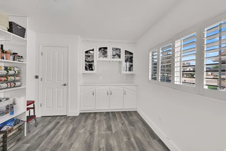 Wood-finish flooring, built-in storage shelving, built-in cabinetry with glass-front uppers, and window shutters