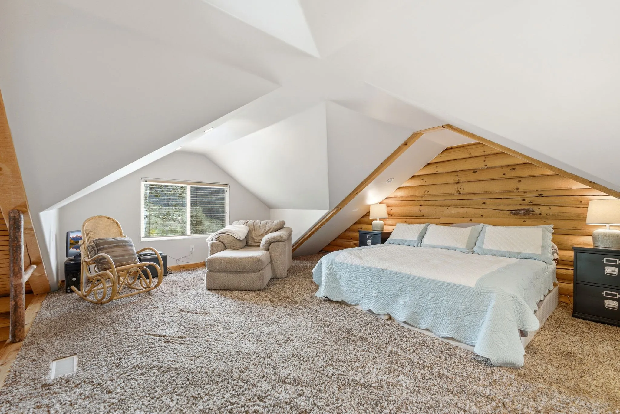 Vaulted ceilings, plank wood wall accent, and sloped white walls with a window