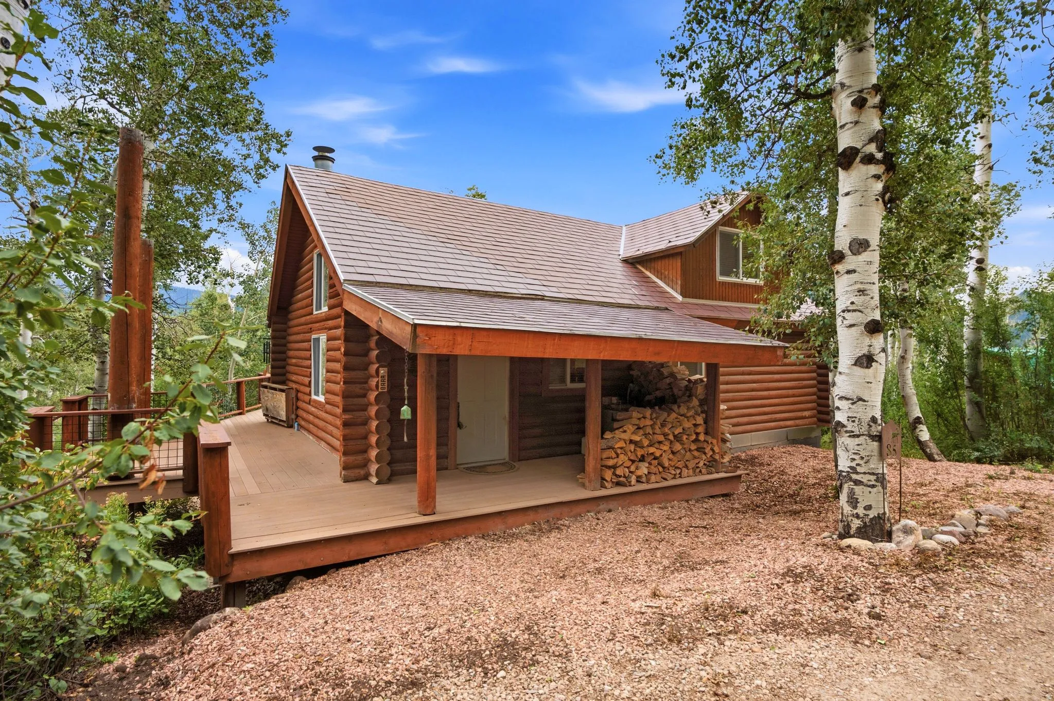 Log cabin exterior with a covered front porch, expansive wood deck, and a prominent chimney