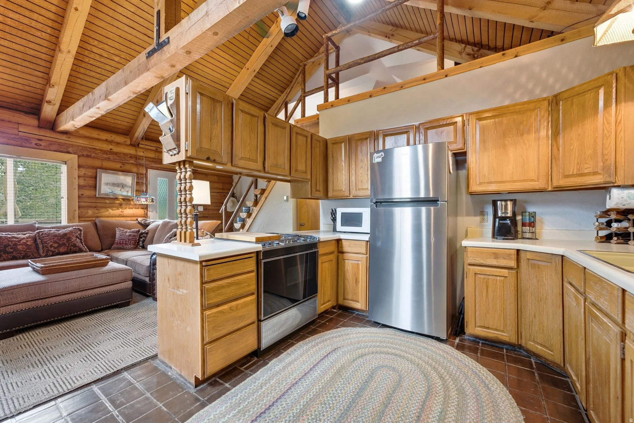 Open-concept kitchen and living area featuring stainless steel appliances, wood cabinetry, a central island with prep space, exposed beam ceiling with skylights, and wood-finish flooring throughout