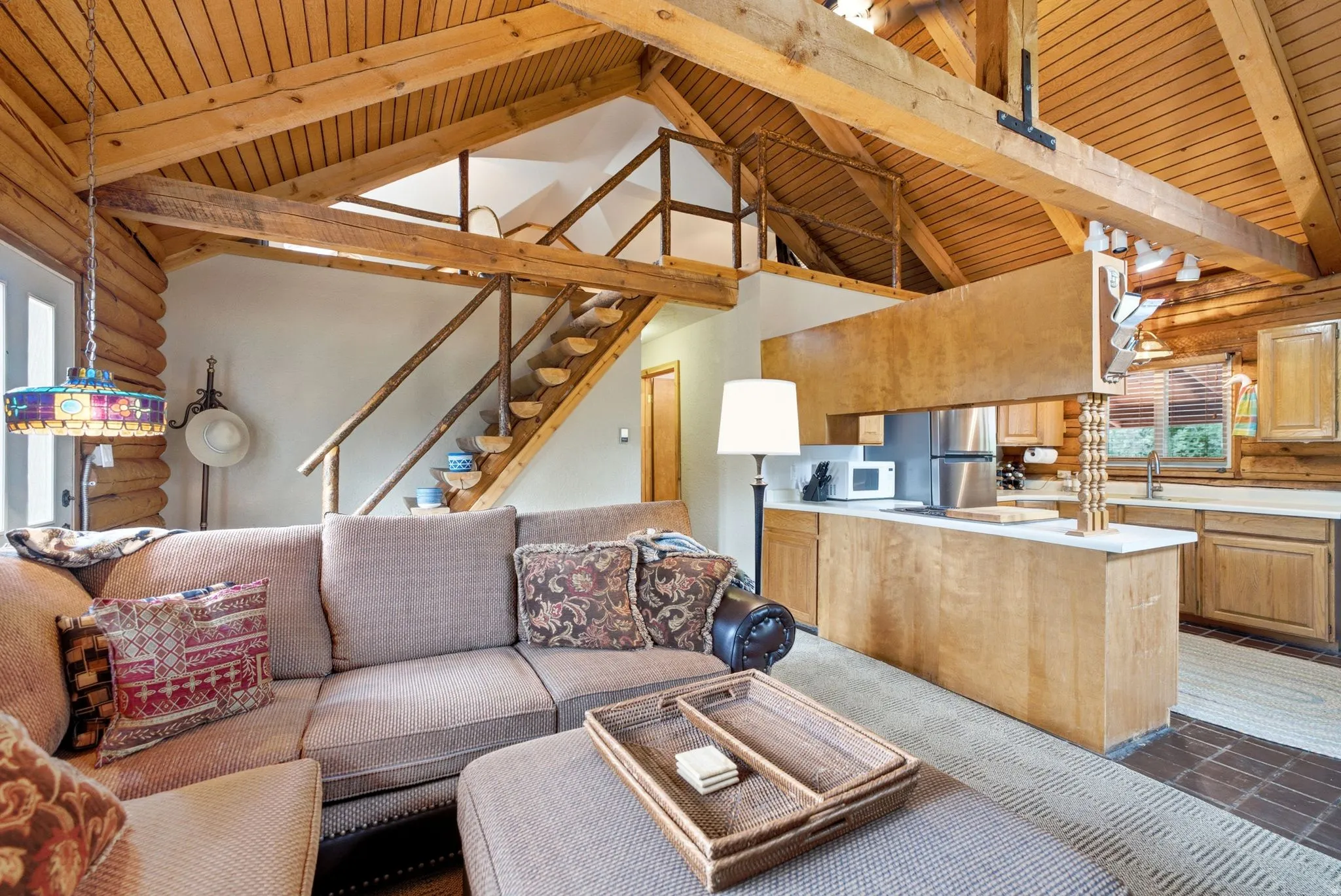 Vaulted wood-paneled ceiling with exposed beams, open loft area, kitchen featuring stainless steel appliances, wood cabinetry, and a white countertop