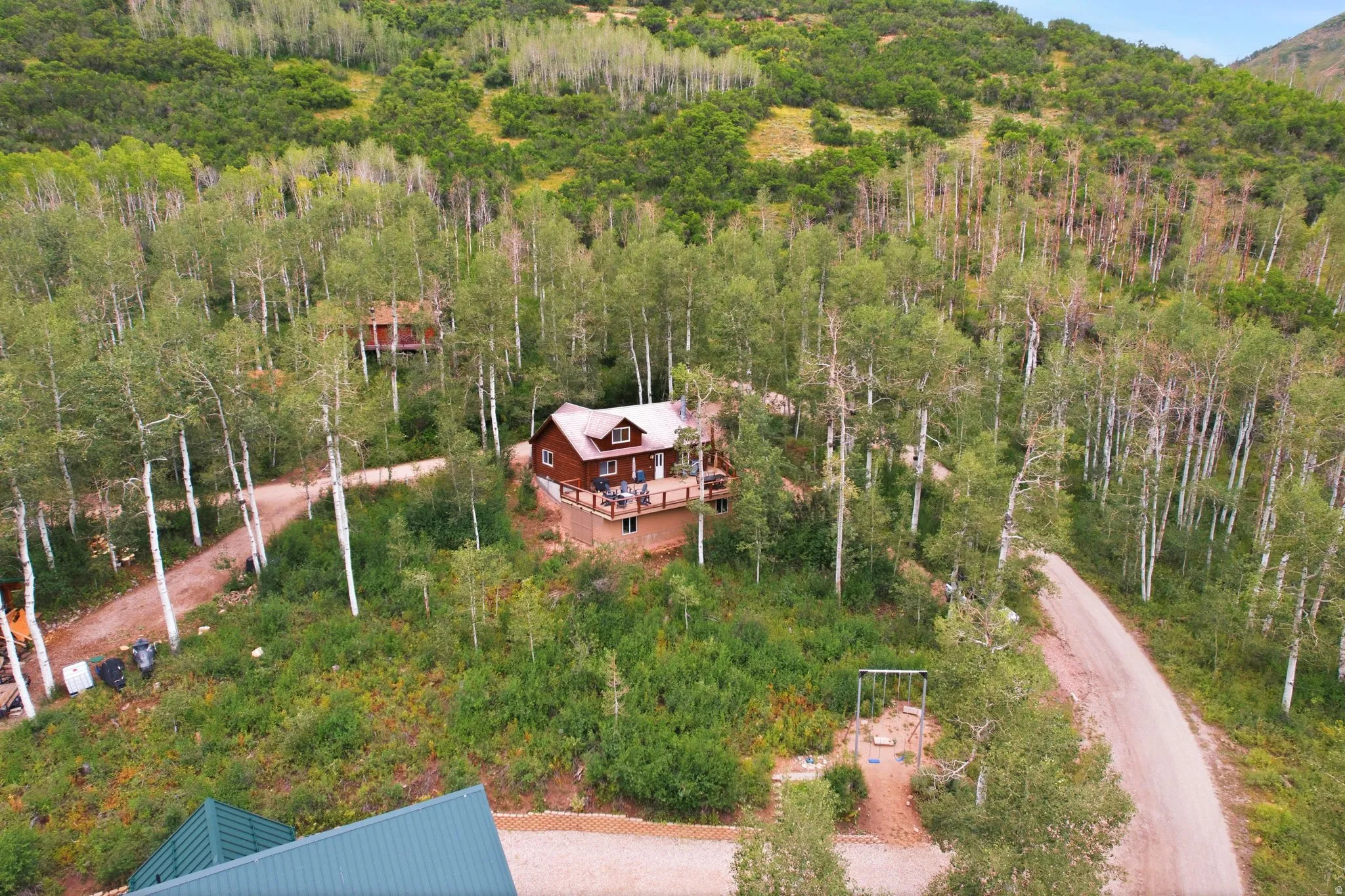 Wood-sided residence featuring a wrap-around deck and dormer windows, surrounded by mature trees