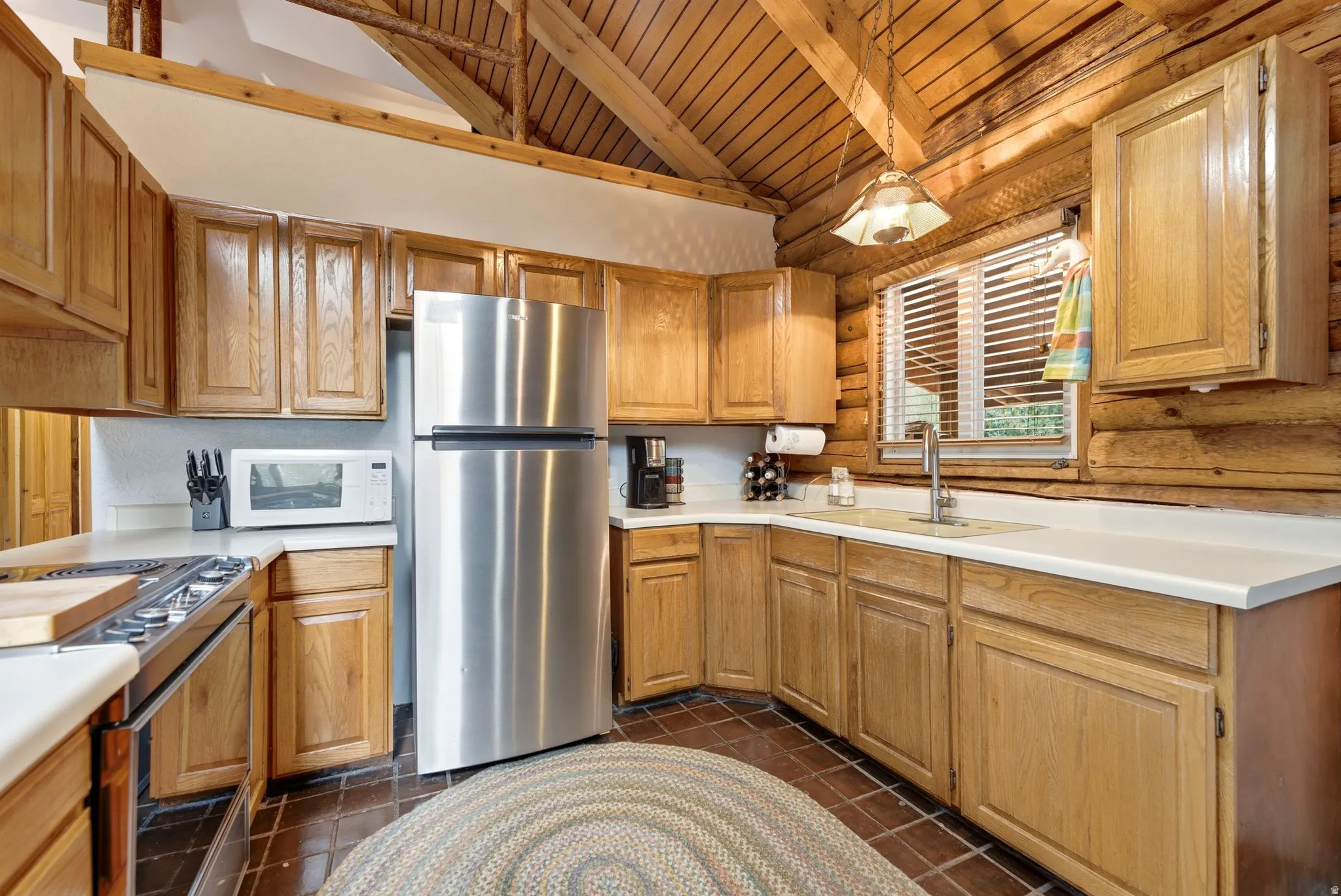Kitchen with wood cabinetry, white countertops, stainless steel appliances, and a wood-paneled ceiling