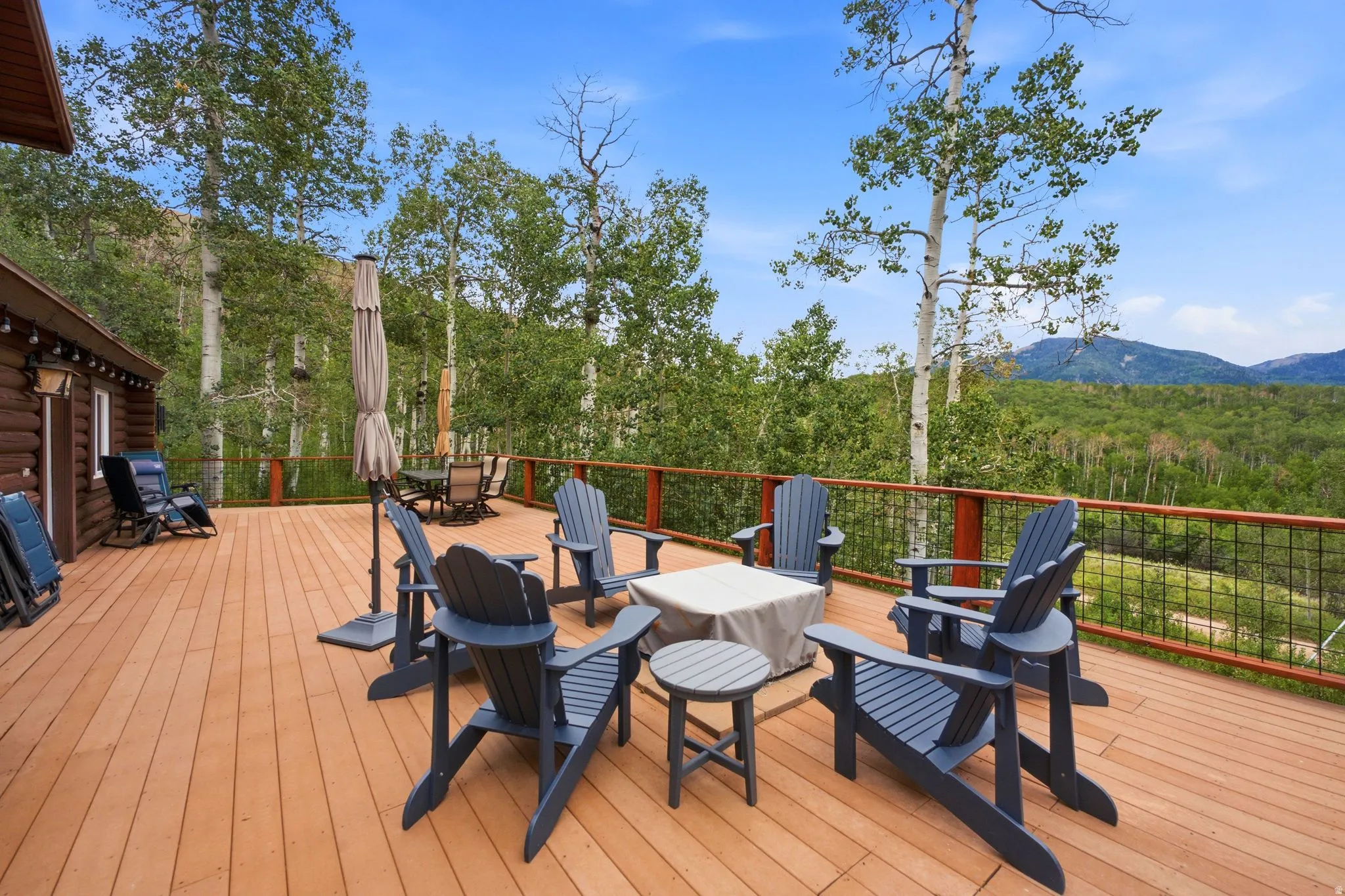 Spacious outdoor deck with wood-finish flooring, metal railing, and a rustic log cabin exterior