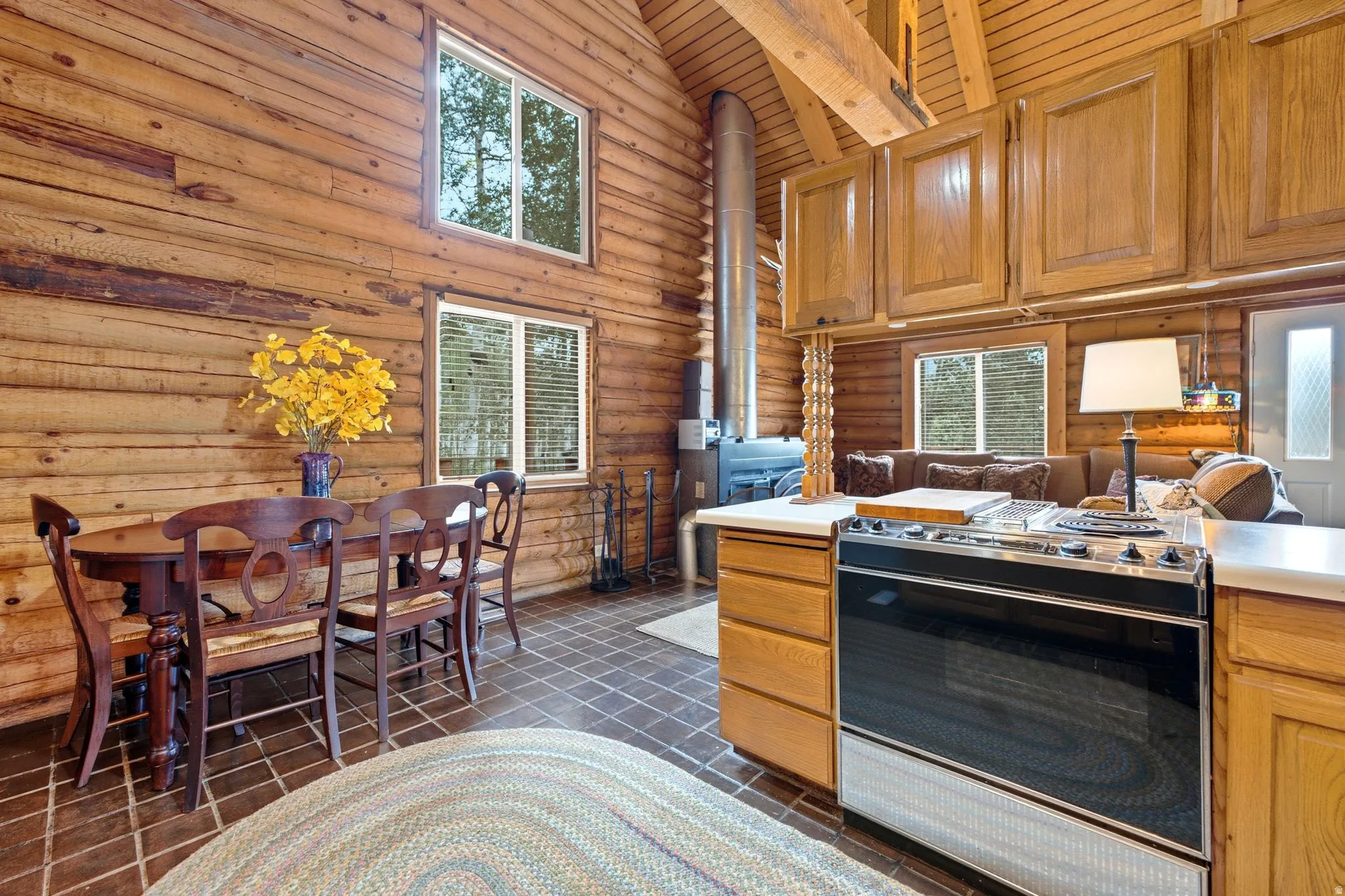 Log-style interior walls, vaulted wood-finish ceiling, tiled flooring, wood-finish cabinetry, and a built-in range