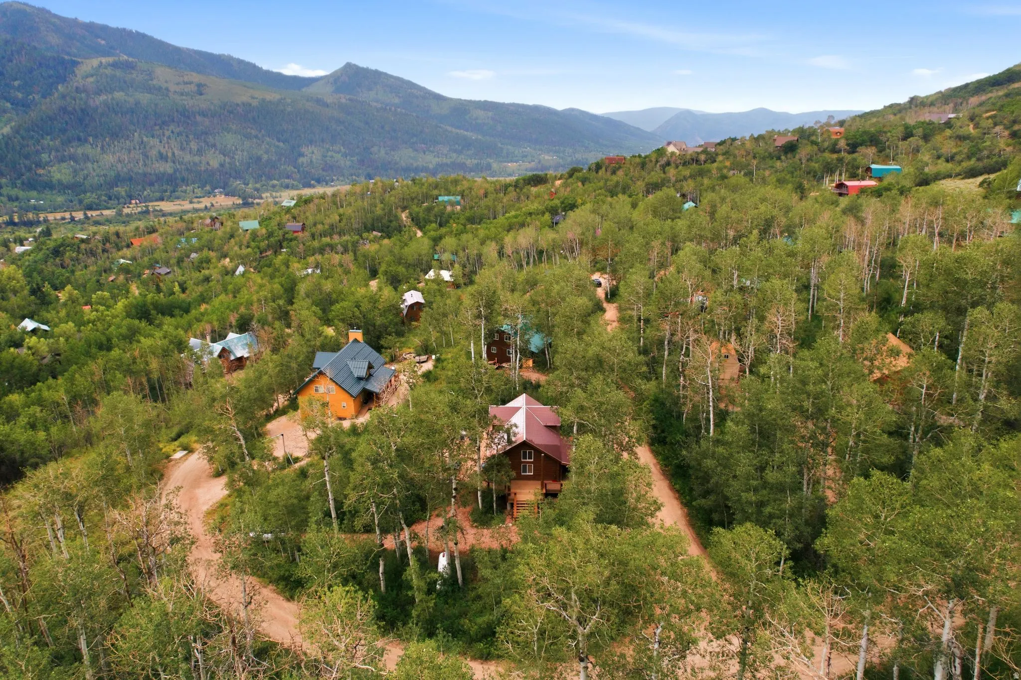 Mountainous backdrop with extensive tree coverage and multiple properties situated on a sloping terrain