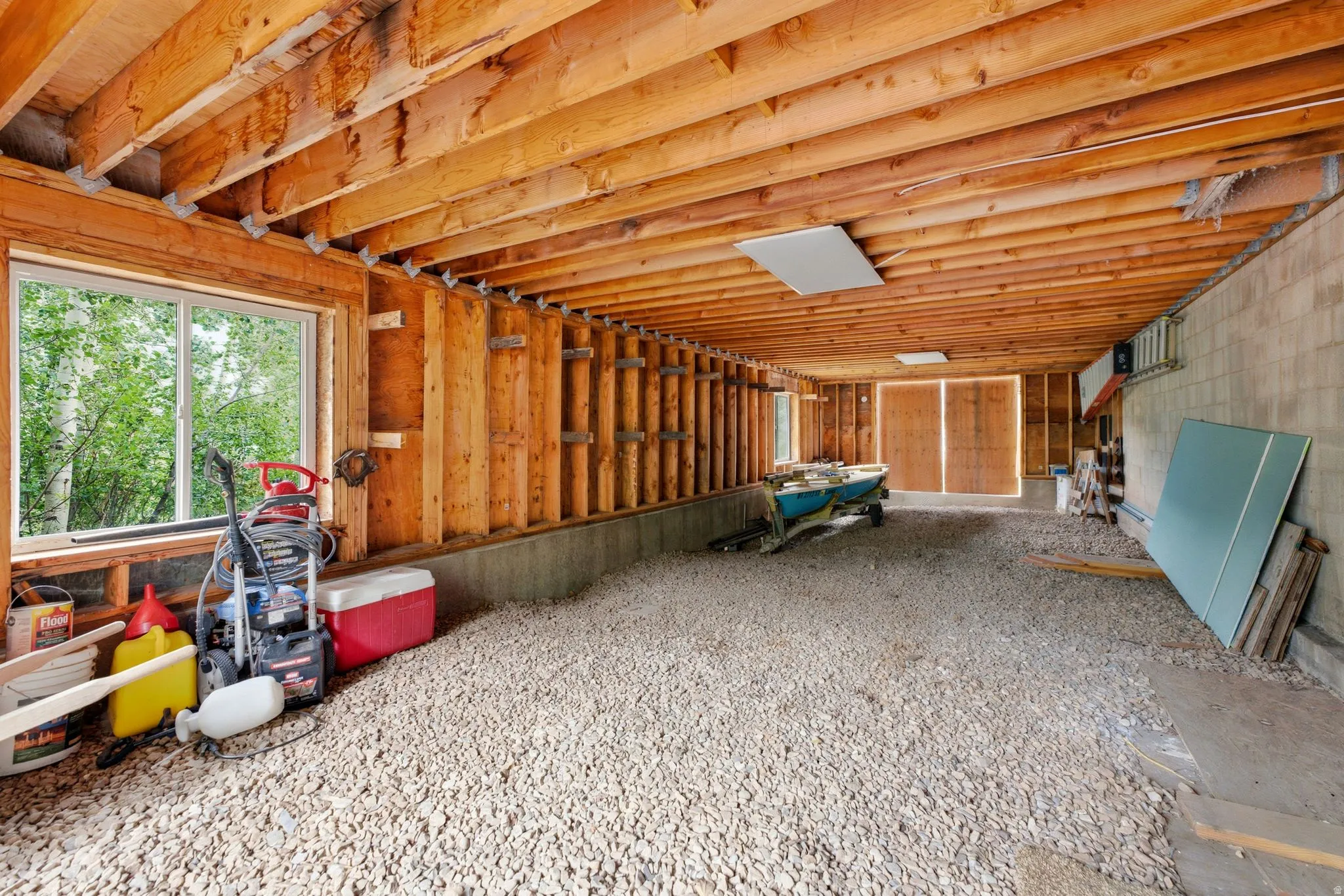 Exposed wood ceiling beams, wood-plank wall construction, concrete block wall, gravel flooring, and a single-pane window