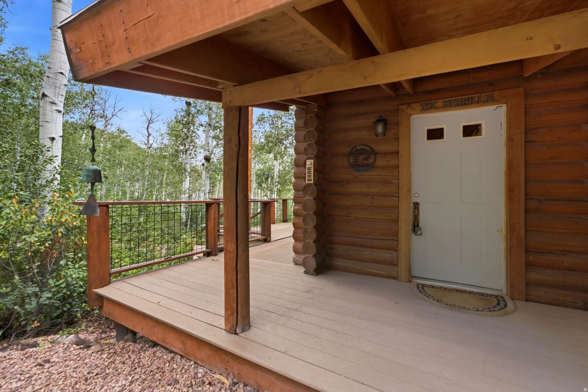 Covered deck with composite decking and wooden support posts, metal cable railing system, and log cabin-style wood siding