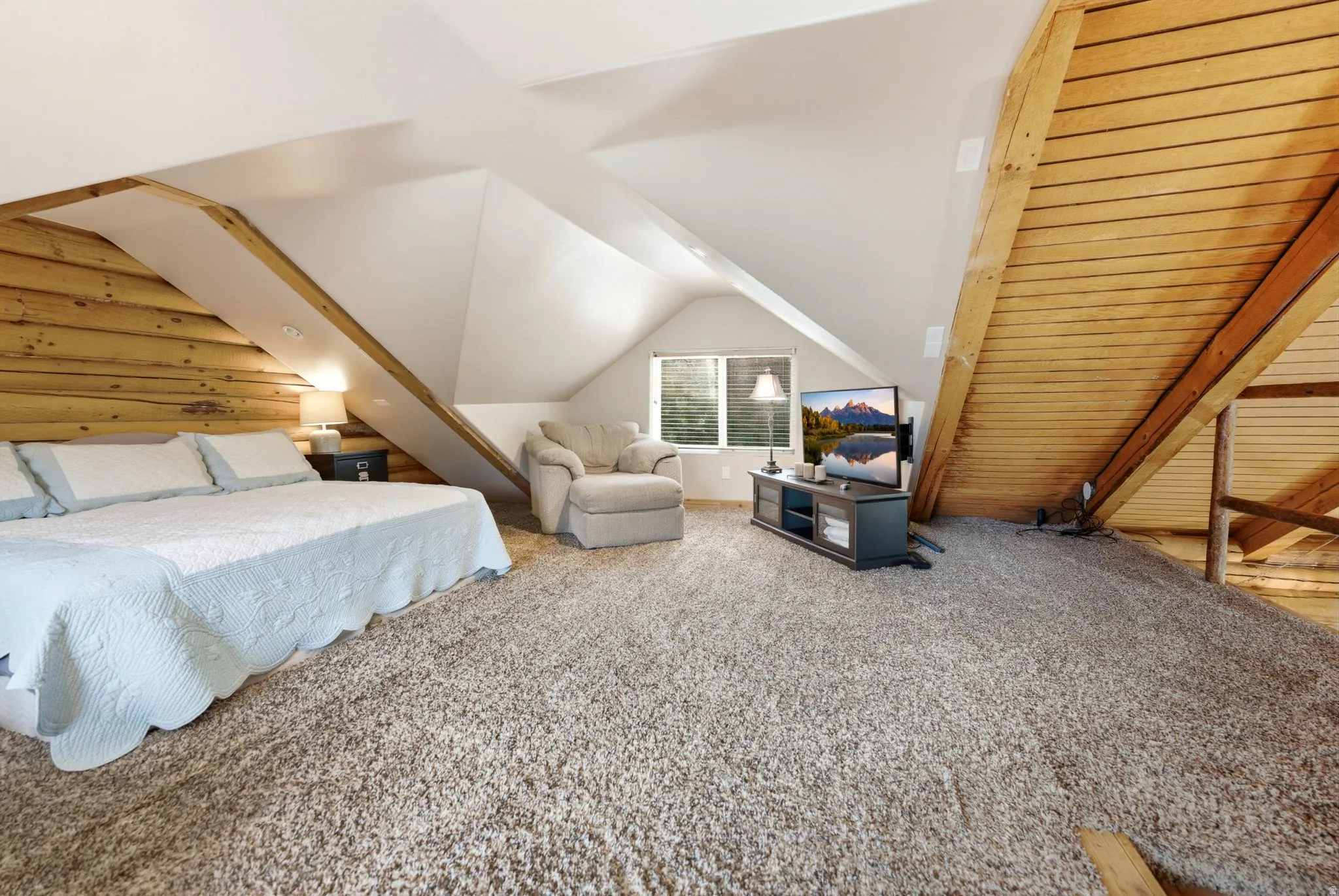 Sloped ceiling with recessed lighting, wood-paneled wall, textured carpet flooring, and a window with horizontal blinds