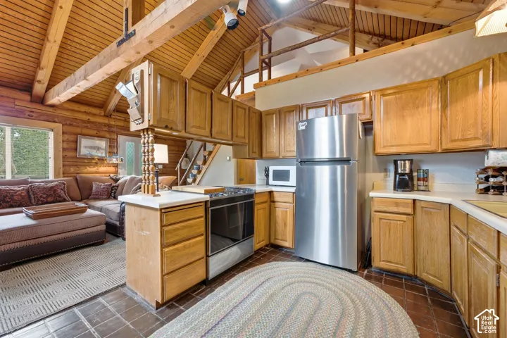 Open-concept kitchen and living area featuring stainless steel appliances, wood cabinetry, a central island with prep space, exposed beam ceiling with skylights, and wood-finish flooring throughout
