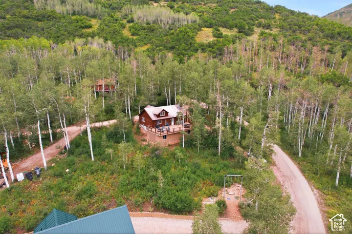 Wood-sided residence featuring a wrap-around deck and dormer windows, surrounded by mature trees