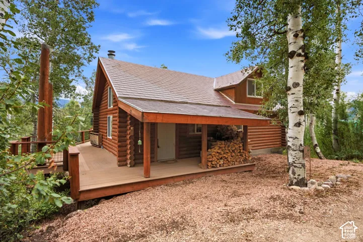 Log cabin exterior with a covered front porch, expansive wood deck, and a prominent chimney