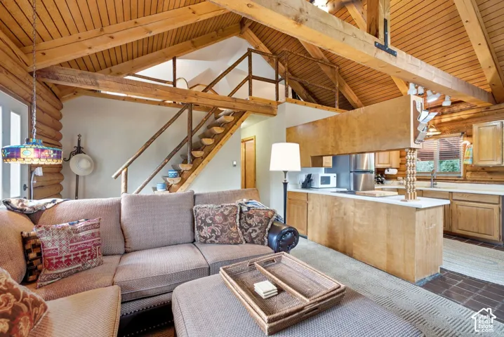 Vaulted wood-paneled ceiling with exposed beams, open loft area, kitchen featuring stainless steel appliances, wood cabinetry, and a white countertop