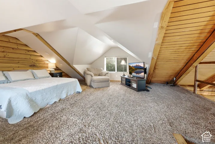 Sloped ceiling with recessed lighting, wood-paneled wall, textured carpet flooring, and a window with horizontal blinds