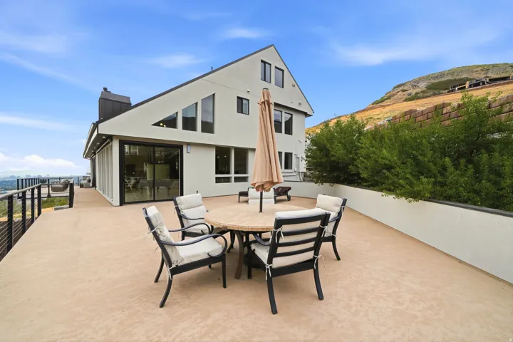 Expansive outdoor deck with a cable railing system, stucco exterior, multiple large windows, and a built-in planter with mature greenery