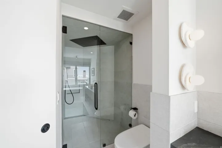 Glass-enclosed shower with matte black fixtures, integrated rainfall showerhead, and light gray wall tiling