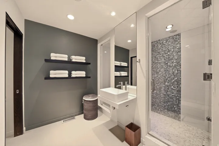Glass-enclosed shower with mosaic tile surround, floating vanity with rectangular vessel sink, full-height mirror, and recessed lighting