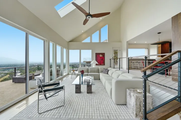Vaulted ceiling with skylight, wood-finish ceiling fan, full-height windows, wood-finish flooring, and a cable railing system with wood-finish handrail