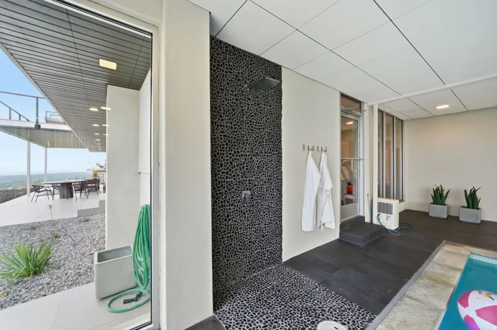Outdoor shower with pebble tile surround and dark tile flooring, featuring an adjacent covered patio