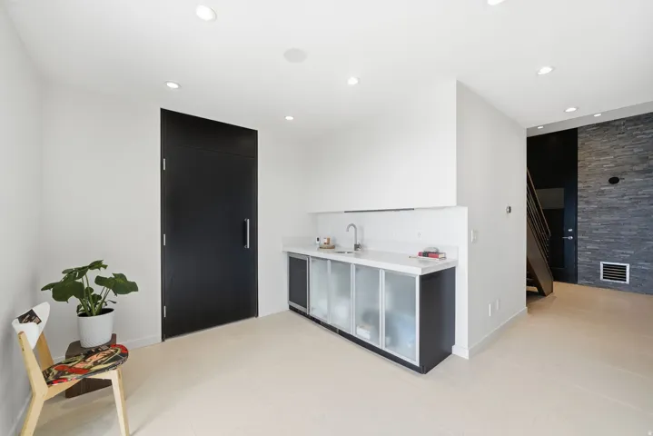 Integrated wet bar with white countertop and tile backsplash, recessed ceiling lighting, and a dark stone-finish accent wall