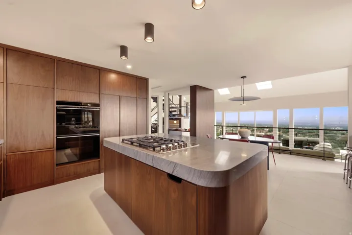 Integrated wood-finish cabinetry, built-in double ovens, and a kitchen island with a gas cooktop