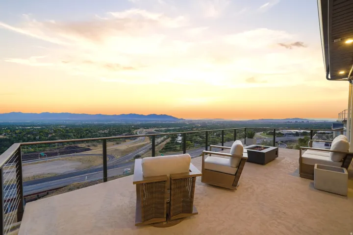 Expansive outdoor patio with glass panel railing, concrete flooring, and a built-in fire pit