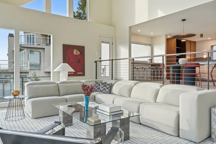 Two-story living area with high ceilings, featuring an upper-level kitchen with wood-finish cabinetry and a breakfast bar, and stainless steel cable railings