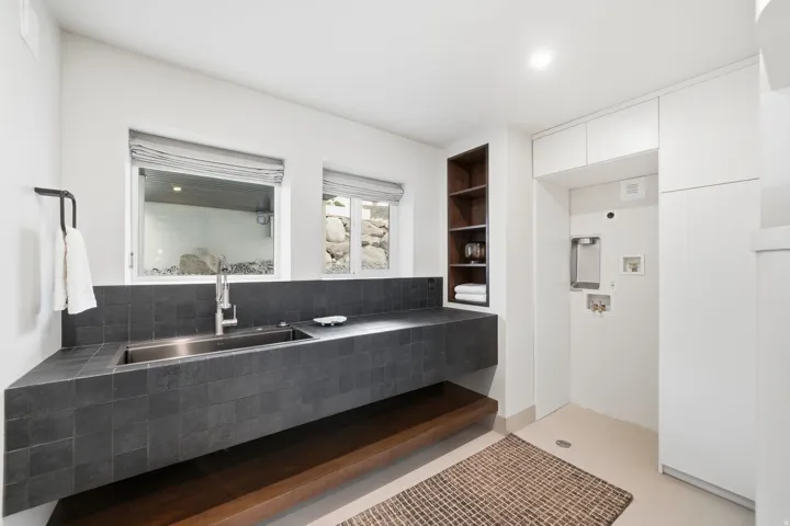 Integrated stainless steel sink, tiled countertop, under-counter wood-finish shelving, built-in open shelving, and recessed lighting