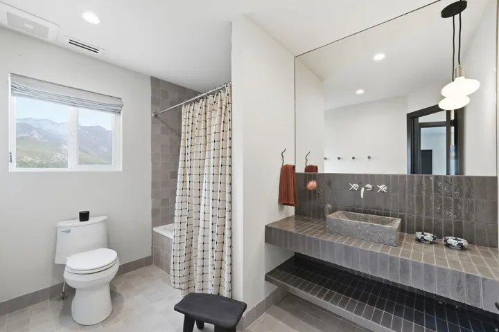 Full-width vanity mirror, modern wall-mounted faucet, vessel sink, and an integrated tiled vanity with shelving