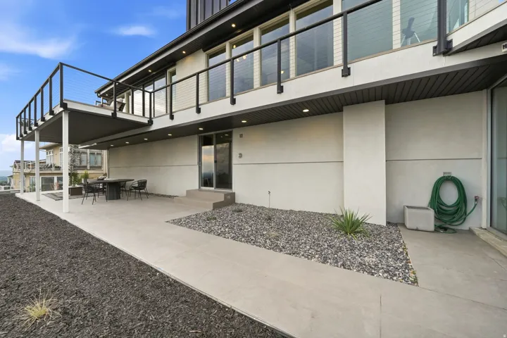 Upper-level deck with cable railing, lower-level concrete patio, steps leading to an entry, and an exterior with a smooth finish