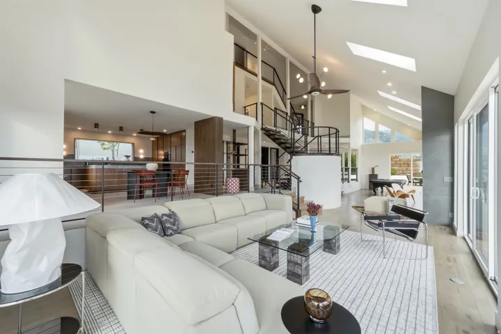 Vaulted ceilings with skylights, wood-finish flooring, open-concept design, spiral staircase with metal railings, and sliding glass doors