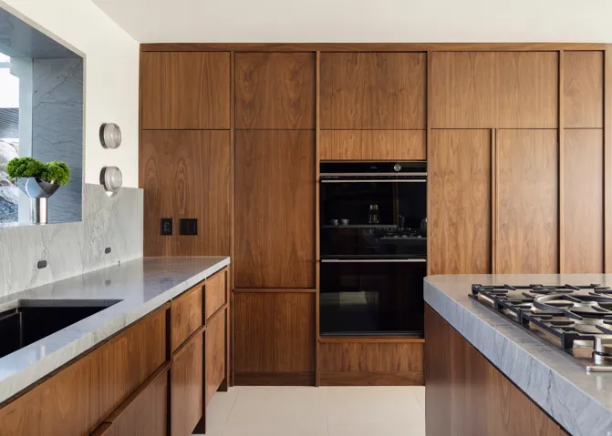 Warm wood-finish cabinetry with integrated appliances, light stone countertops, and a built-in double oven